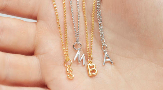 tiny initial letter necklaces in silver and gold in the palm of the hand