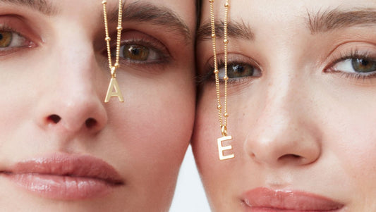 sisters posing with matching initial necklaces in front of their faces